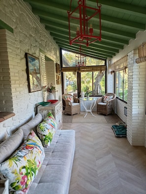 A room with a herringbone floor, a sofa with floral cushions, wicker chairs, and a red hanging lantern.