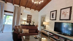 Una sala de estar acogedora con un sofá de cuero marrón, una mesa de centro de vidrio, un televisor y cuadros en la pared.