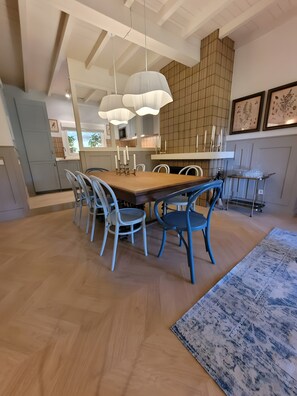 A dining area with a wooden table, blue chairs, hanging pendant lights, and a patterned rug.