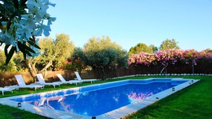 Una piscina rectangular con borde de azulejos, rodeada por un césped y sillas de descanso blancas.