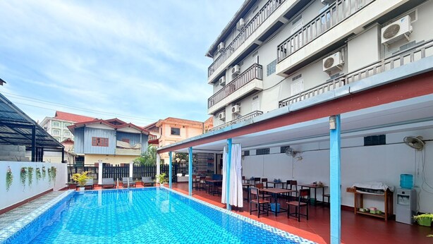 Una piscina con pavimento piastrellato, area salotto esterna e zona coperta con tavoli e sedie.