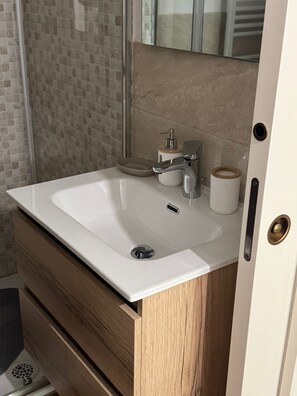 A bathroom with a white sink, a mirror, a soap dispenser, and a toilet paper holder.