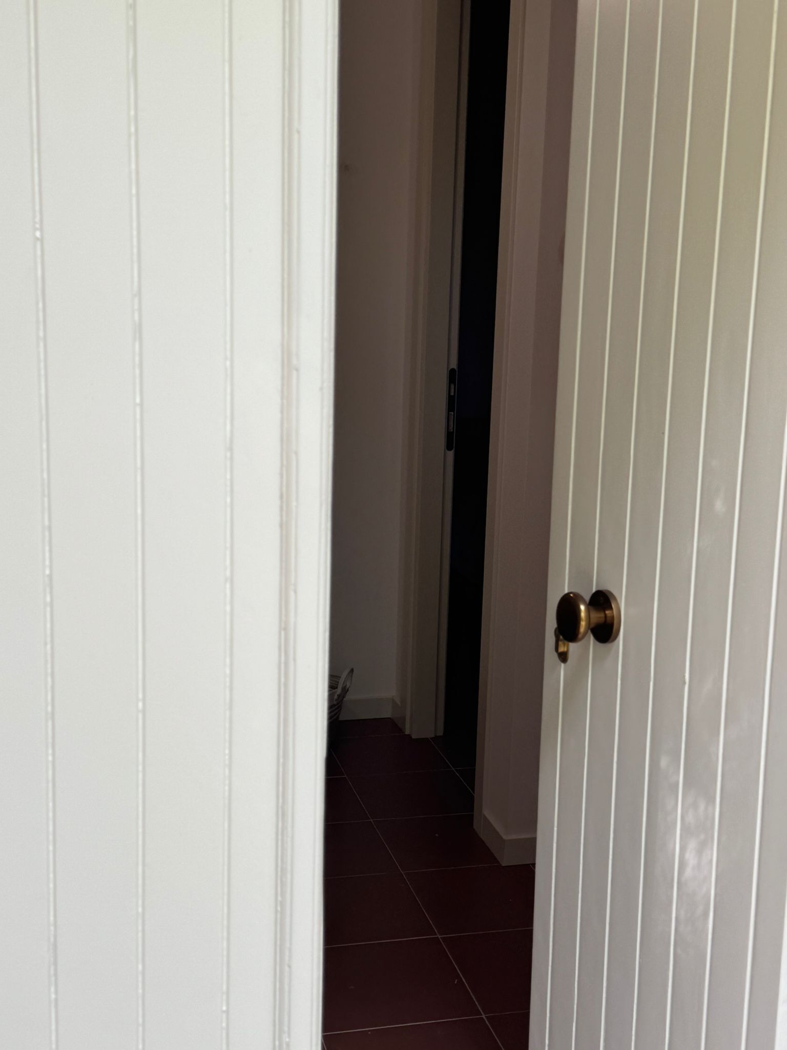 Ein Flur mit einer weißen Tür, einer dunklen Wand und einem Fliesenboden.