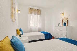 Ein Schlafzimmer mit zwei Betten, einem Schminktisch, einem Spiegel und einem Fenster mit Vorhängen.