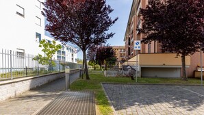 Un sendero pavimentado, una bicicleta, un edificio con un letrero de estacionamiento y un árbol con hojas rojas.