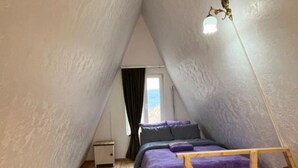 A small, triangular attic bedroom with a bed, a wooden bench, and a hanging light fixture. - Metsadzor Resort, Areni (Areni)