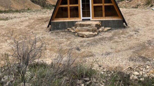 A triangular wooden structure with a central door and a small window, surrounded by a dry, rocky landscape with mountains in the background. - Metsadzor Resort, Areni (Areni)
