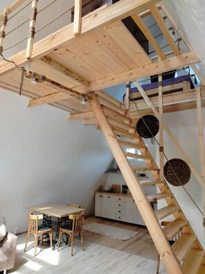 Ein Loft-Zimmer mit einer Holztreppe, einem Esstisch und einer KĂŒchenzeile.
