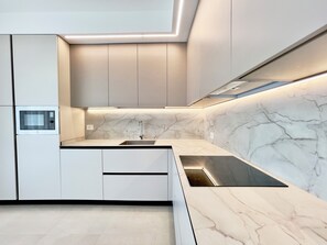 Eine moderne Küche mit weißen Schränken, einer eingebauten Mikrowelle, einer Edelstahl-Spüle und einer Marmor-Spritzschutzwand.