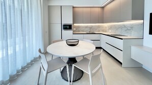 Et moderne køkken med indbygget ovn, marmor bagplade og et rundt spisebord med stole.