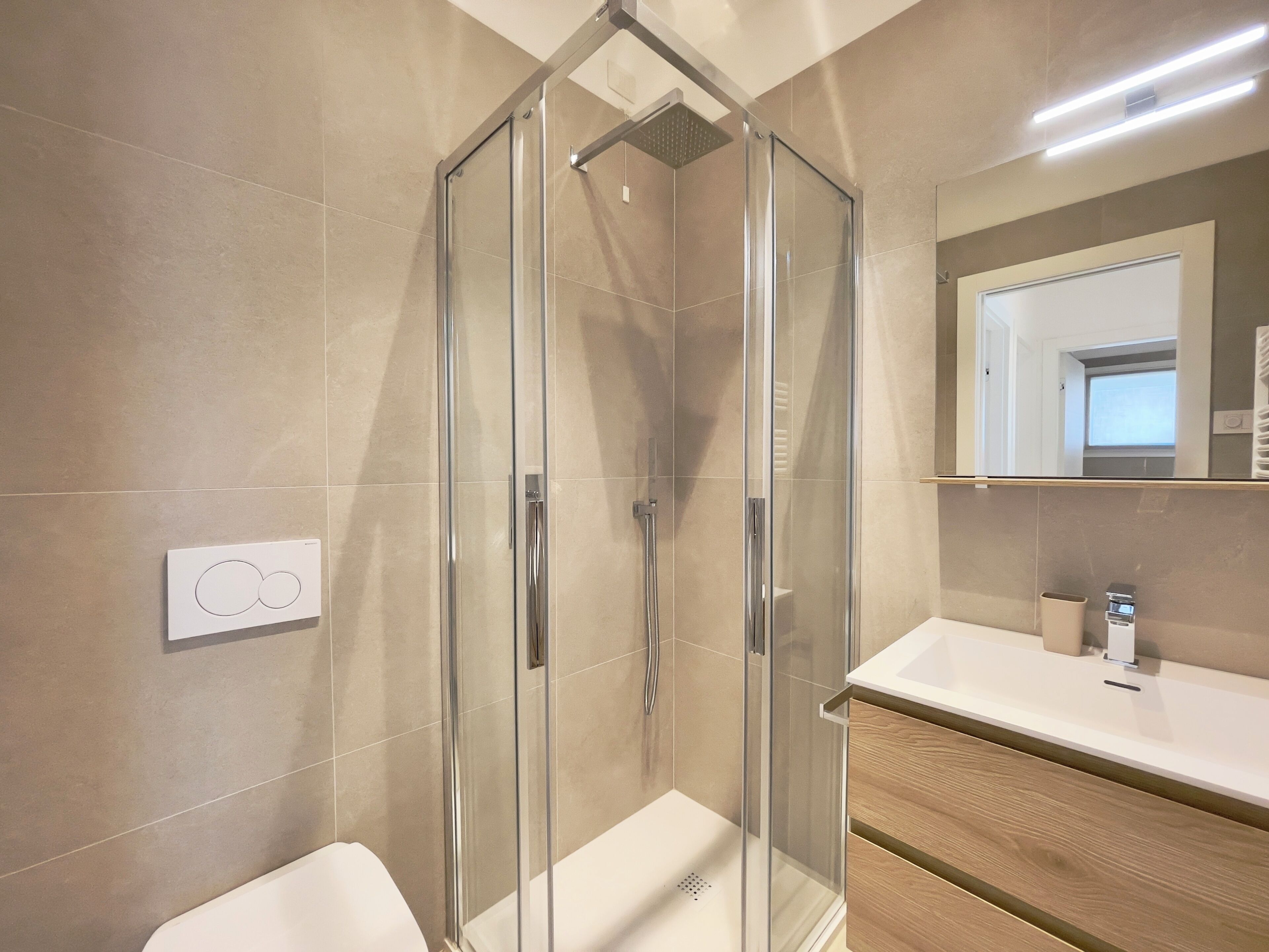 Ein modernes Badezimmer mit einer begehbaren Glasdusche, einem weißen Waschbecken und einem Holzlagerraum.