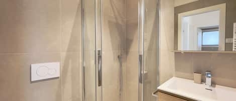 Ein modernes Badezimmer mit einer begehbaren Glasdusche, einem weißen Waschbecken und einem Holzlagerraum.