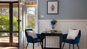 Ein Zimmer mit Tisch, zwei Stühlen, einer Blumenvase und einem gerahmten Bild an der Wand.