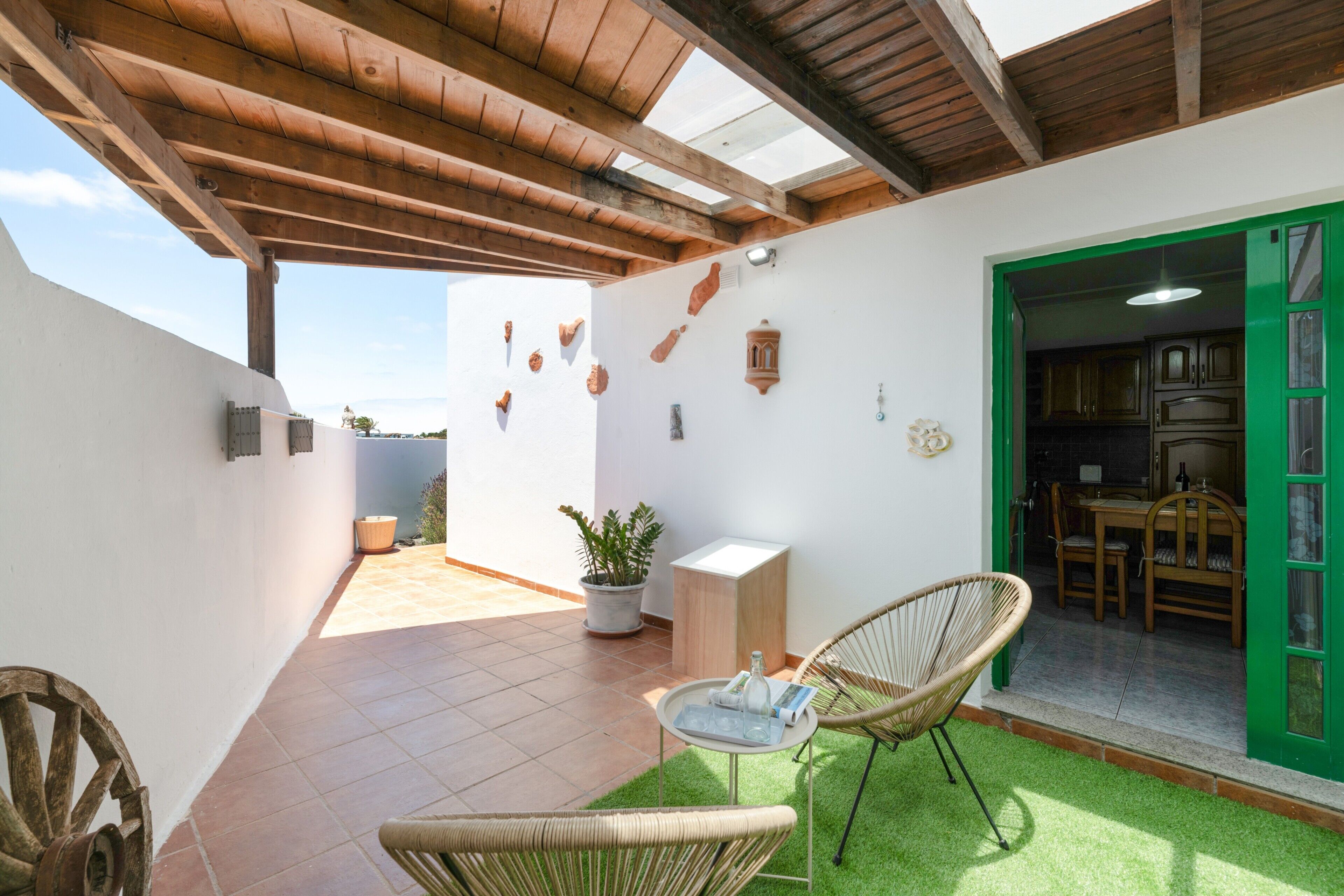 Un patio con techo de madera, una zona de comedor con puerta verde y una planta en maceta.