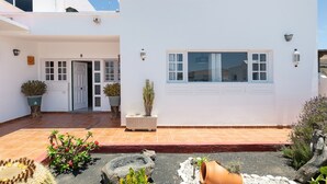 Un edificio blanco con un patio empedrado, plantas en macetas y una jardinera de piedra.