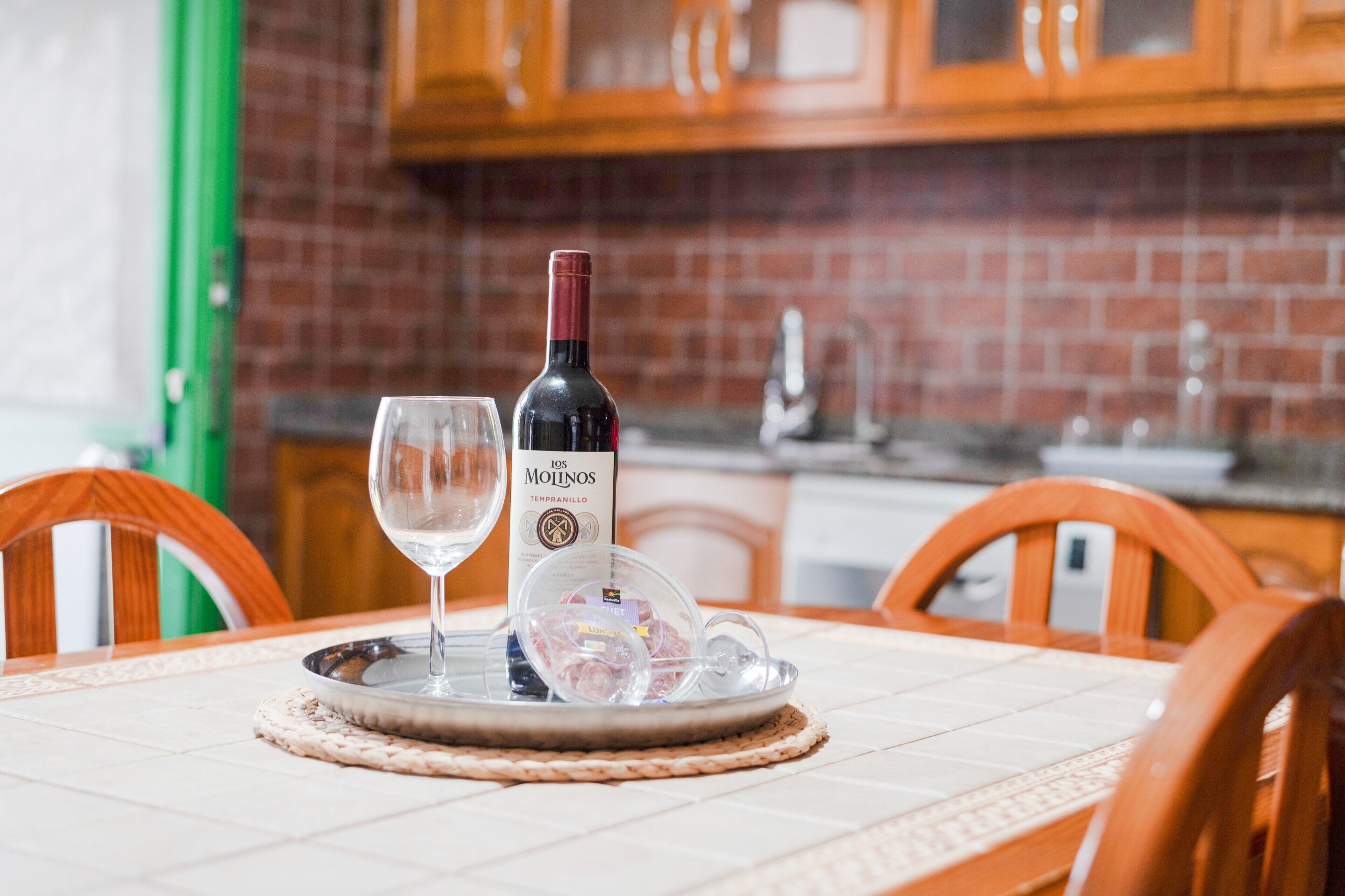 A dining table with a wine bottle, a glass, and a glass container in a kitchen setting.