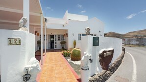Un edificio blanco con un acceso con tejas, un cactus y una estatua de una figura.