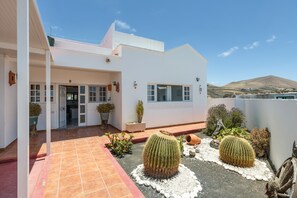 A modern white building with a covered patio, large cacti, and a mountain in the background. - Holiday Home 'Unit 2' with Mountain View and Wi-Fi (Uga)