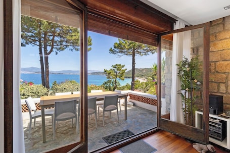Una stanza con un'ampia porta vetrata che si apre su una terrazza esterna, arredata con un tavolo, sedie, un muro in pietra e un camino.. Villa 'Aster' con vista mare, Wi-Fi e aria condizionata