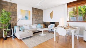Een moderne woonkamer met een stenen muur, een open haard, een eethoek met witte meubels en een groot raam met planten.