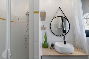 A modern bathroom with a glass shower enclosure, a white sink with a black faucet, a wooden vanity, a mirror with a black frame, and a green vase on the vanity. - Villa 'Aster' with Sea View, Wi-Fi and Air Conditioning (Coti-Chiavari)