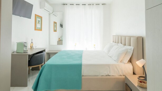 Ett hotellrum med en säng, ett skrivbord, en stol och ett fönster med gardiner.