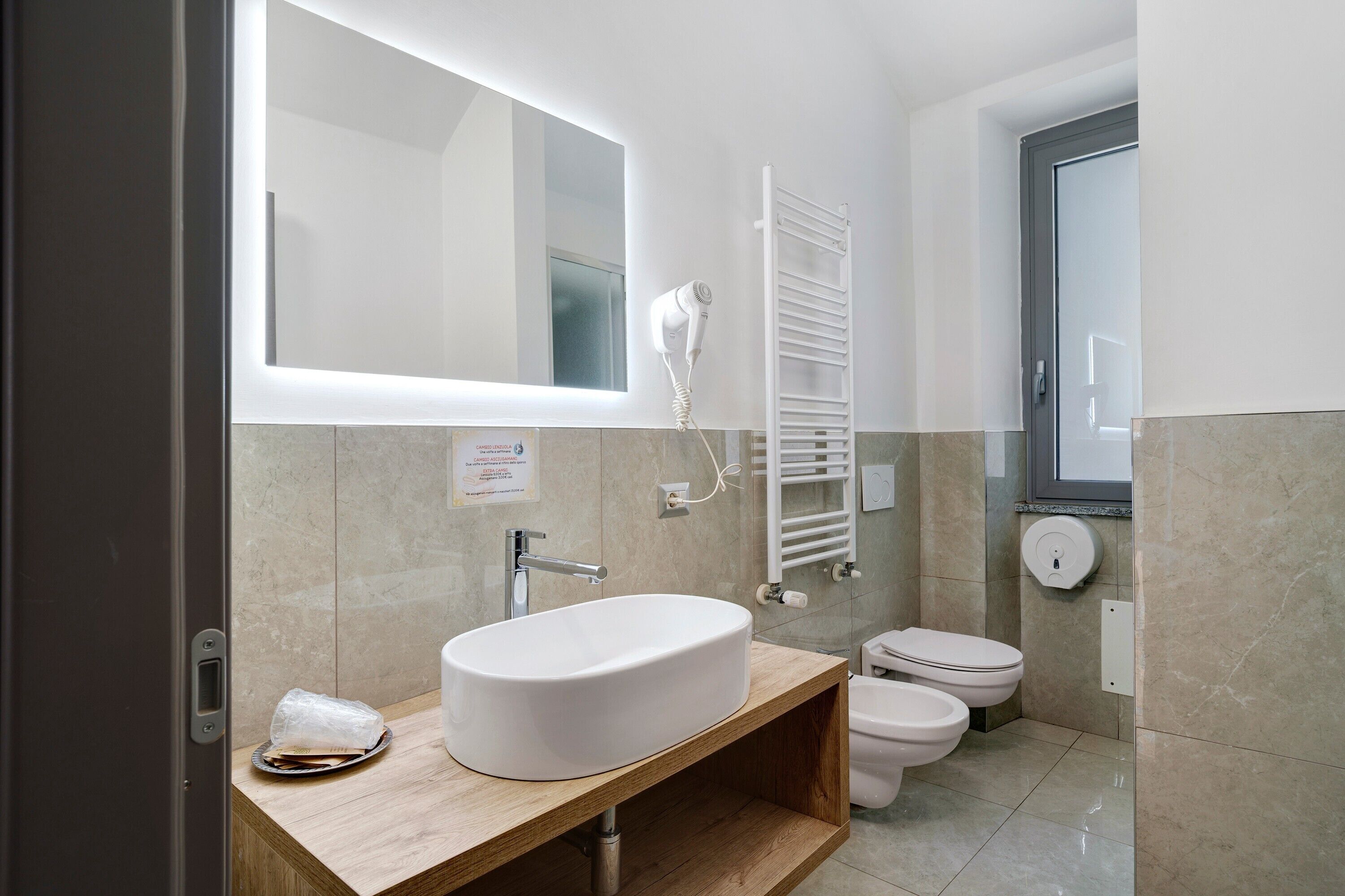 Ein modernes Badezimmer mit einem großen Spiegel, einem weißen Waschbecken, einem Handtuchhalter und einer Toilette.
