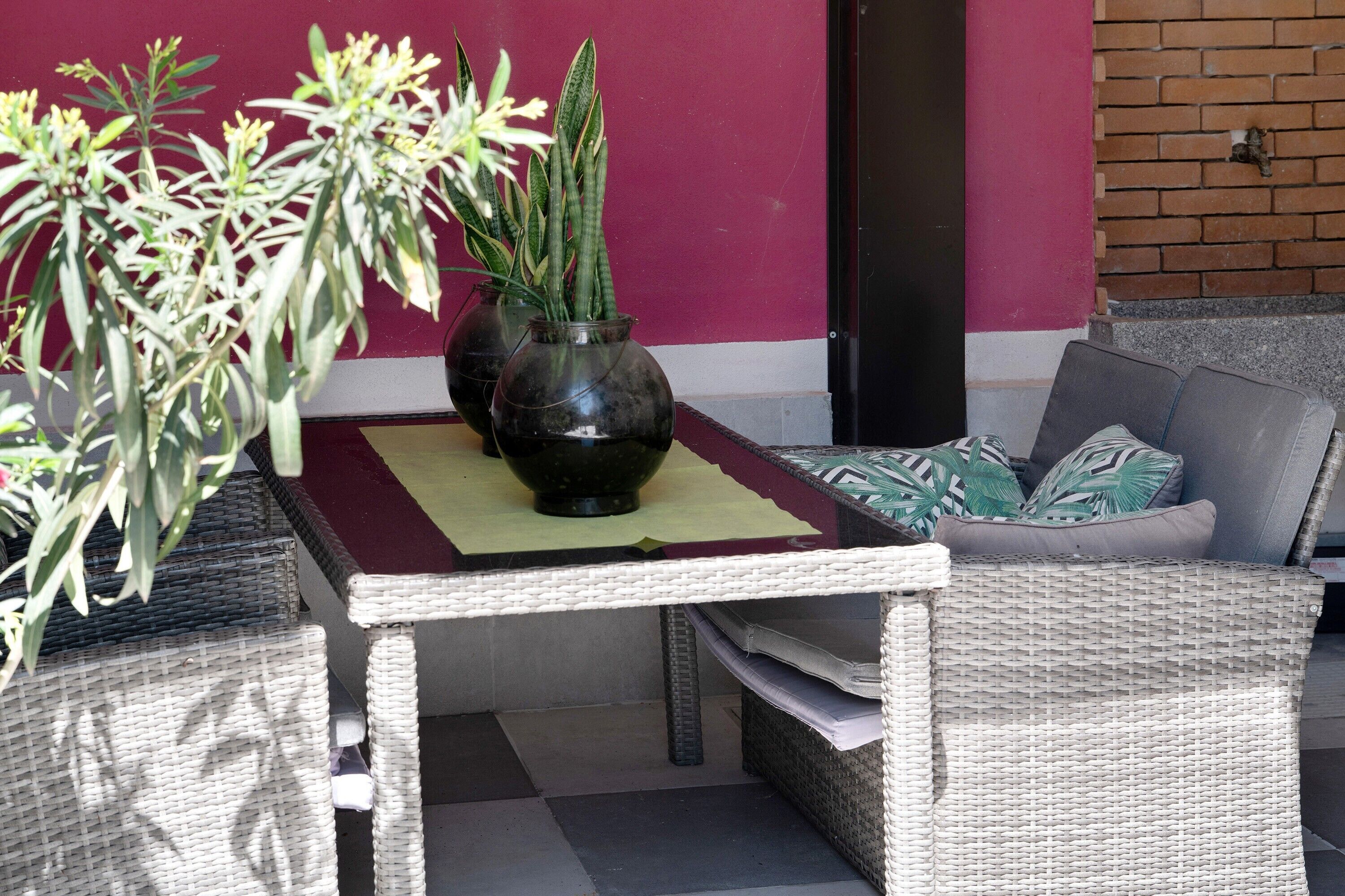 A wicker table with a vase of plants, a sofa with cushions, and a red wall.