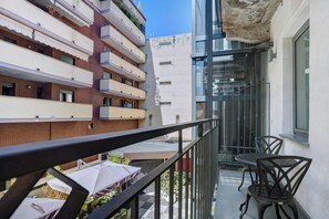 A balcony with a table and chairs, a view of adjacent buildings, and a clear sky.