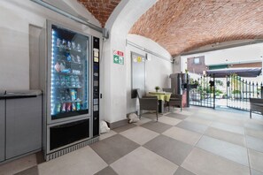 Una máquina expendedora de bebidas, un área de descanso con mesas y sillas, y un techo de ladrillo.