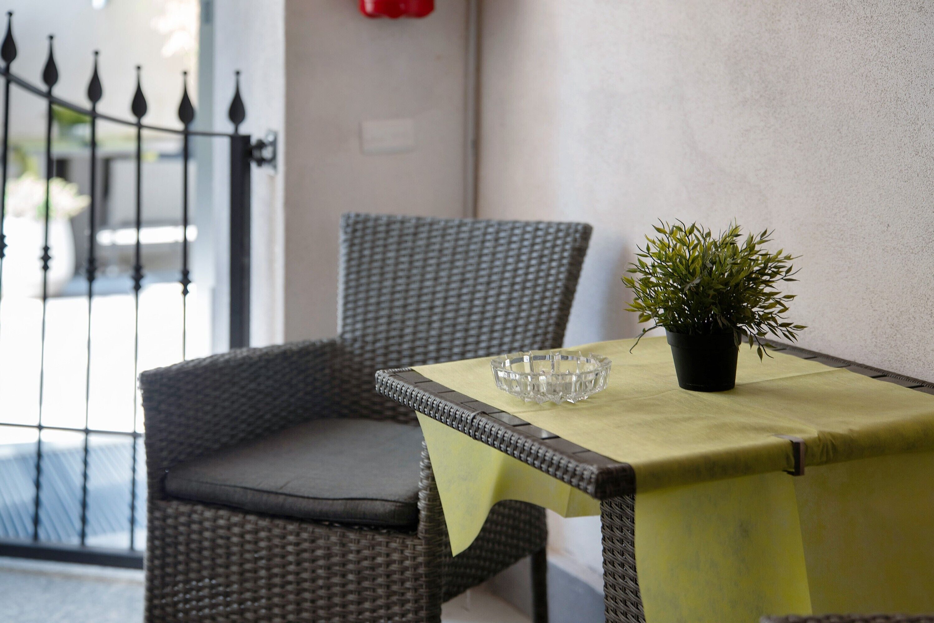 A wicker chair with a cushion, a small potted plant, and a glass bowl on a table with a yellow tablecloth.