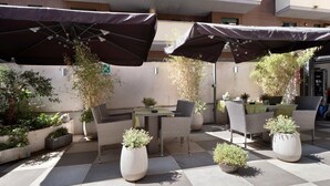 Een terras buiten met zwart-wit geruit vloer, rieten meubels en potplanten.