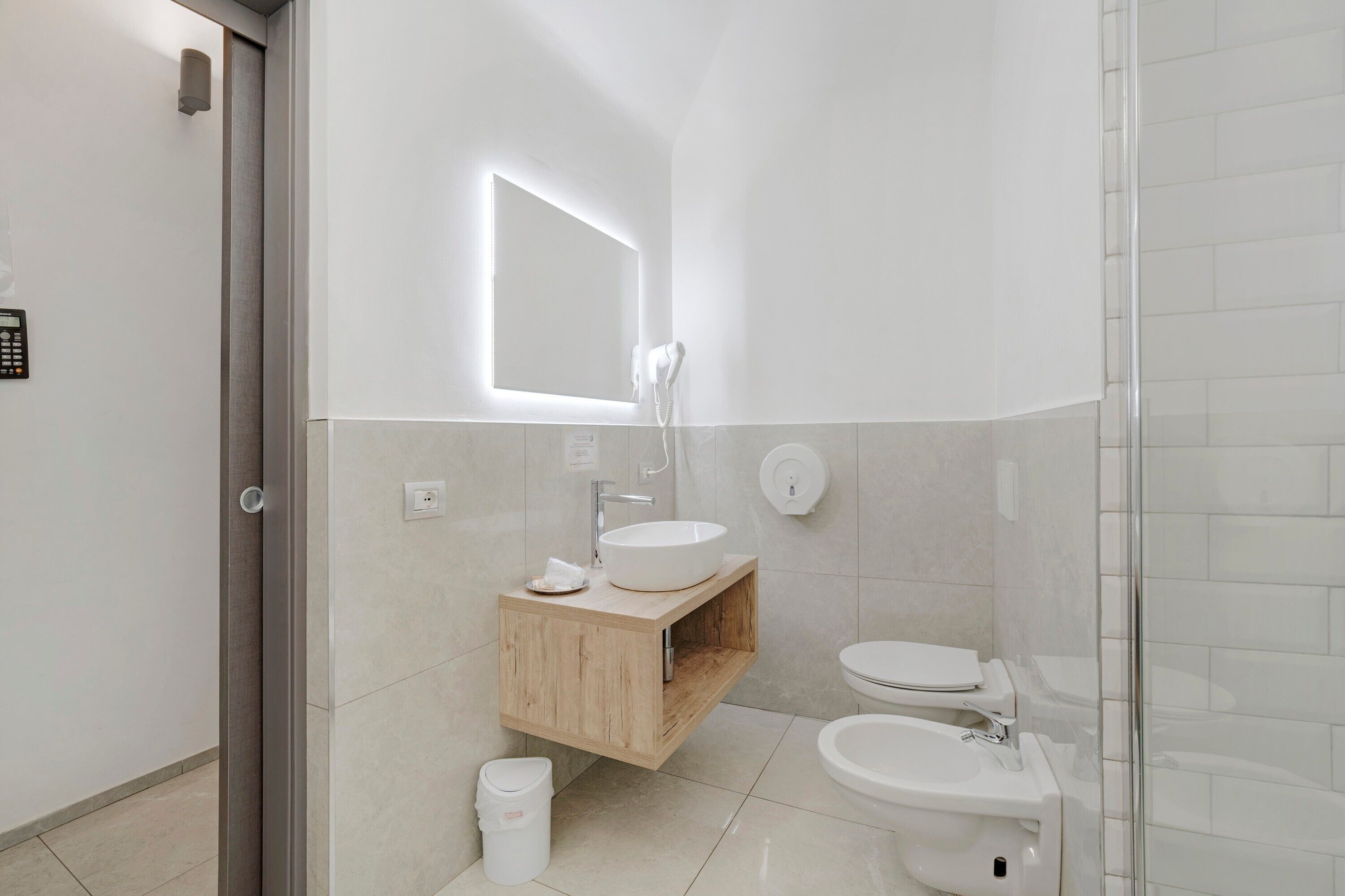 A modern bathroom with a wooden vanity, a large mirror, a sink, a toilet, and a shower area.