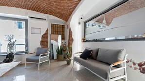 Een moderne woonkamer met een bakstenen plafond, een bank, een stoel, een tafel en een potplant.
