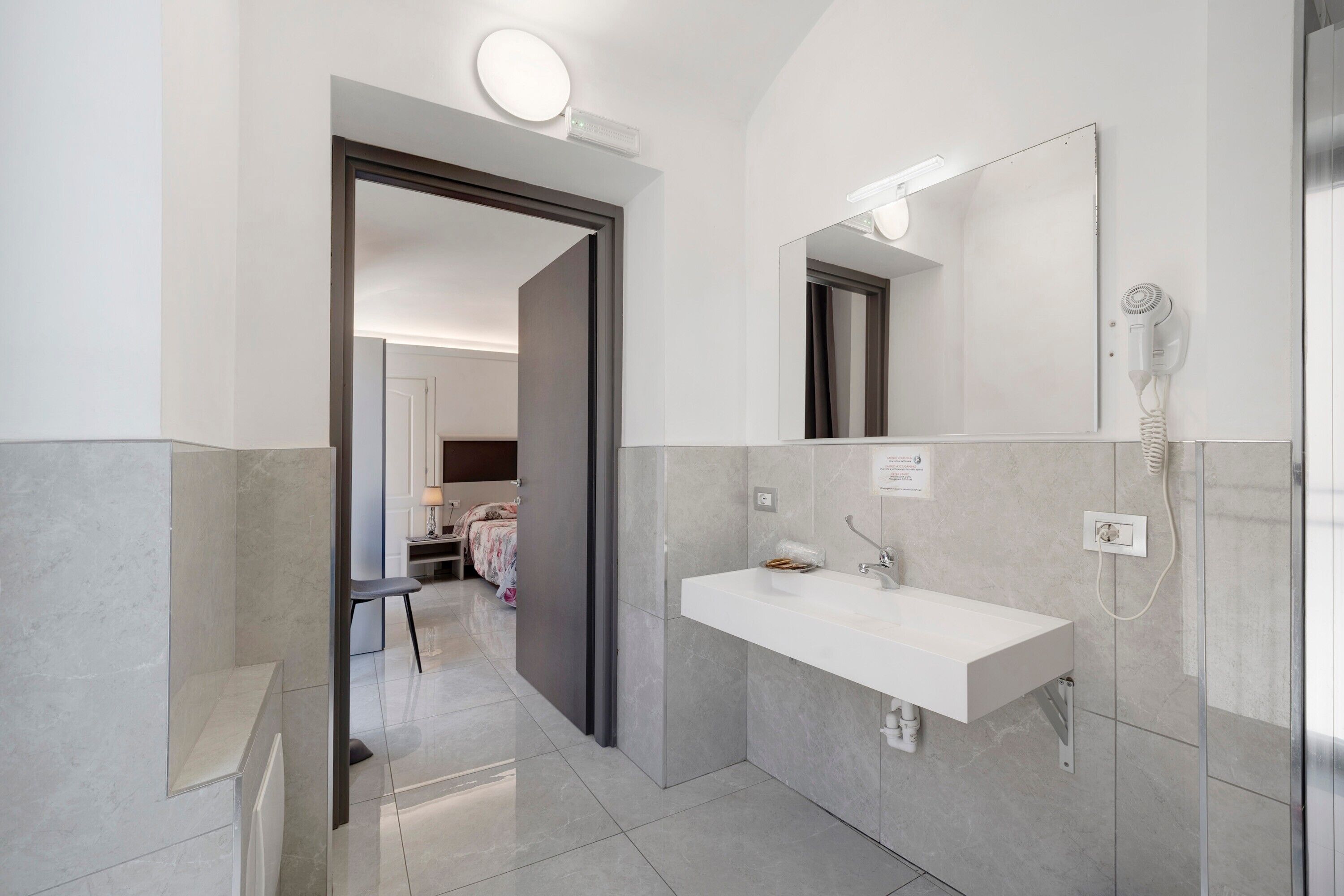 Une salle de bain moderne avec un grand miroir, un lavabo blanc et un espace douche.