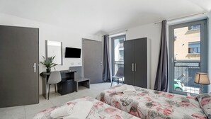 Hotelkamer met twee bedden, een bureau, een stoel, een televisie en een balkon met uitzicht op de stad.