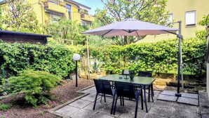 Um pátio externo com uma mesa e cadeiras, rodeado por vegetação e um edifício ao fundo.