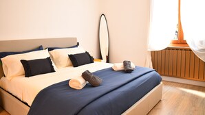 Cama bem arrumada com almofadas, mesa de cabeceira e janela com cortinas.