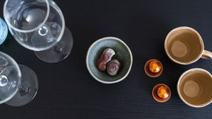 A top-down view of a dining table with various items including empty wine glasses, a bowl with two snail shells, and two small cups with a decorative lid.