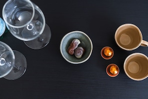 A top-down view of a dining area with empty wine glasses, a bowl with two decorative items, and two cups on a dark surface.
