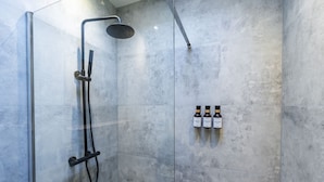 A shower with a handheld showerhead and a wall-mounted faucet, and three bottles of shampoo on the wall.