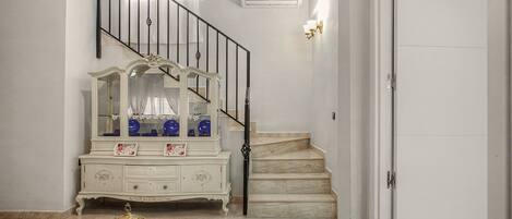 A staircase with a white wall, a white door, and a white dresser with glass doors.