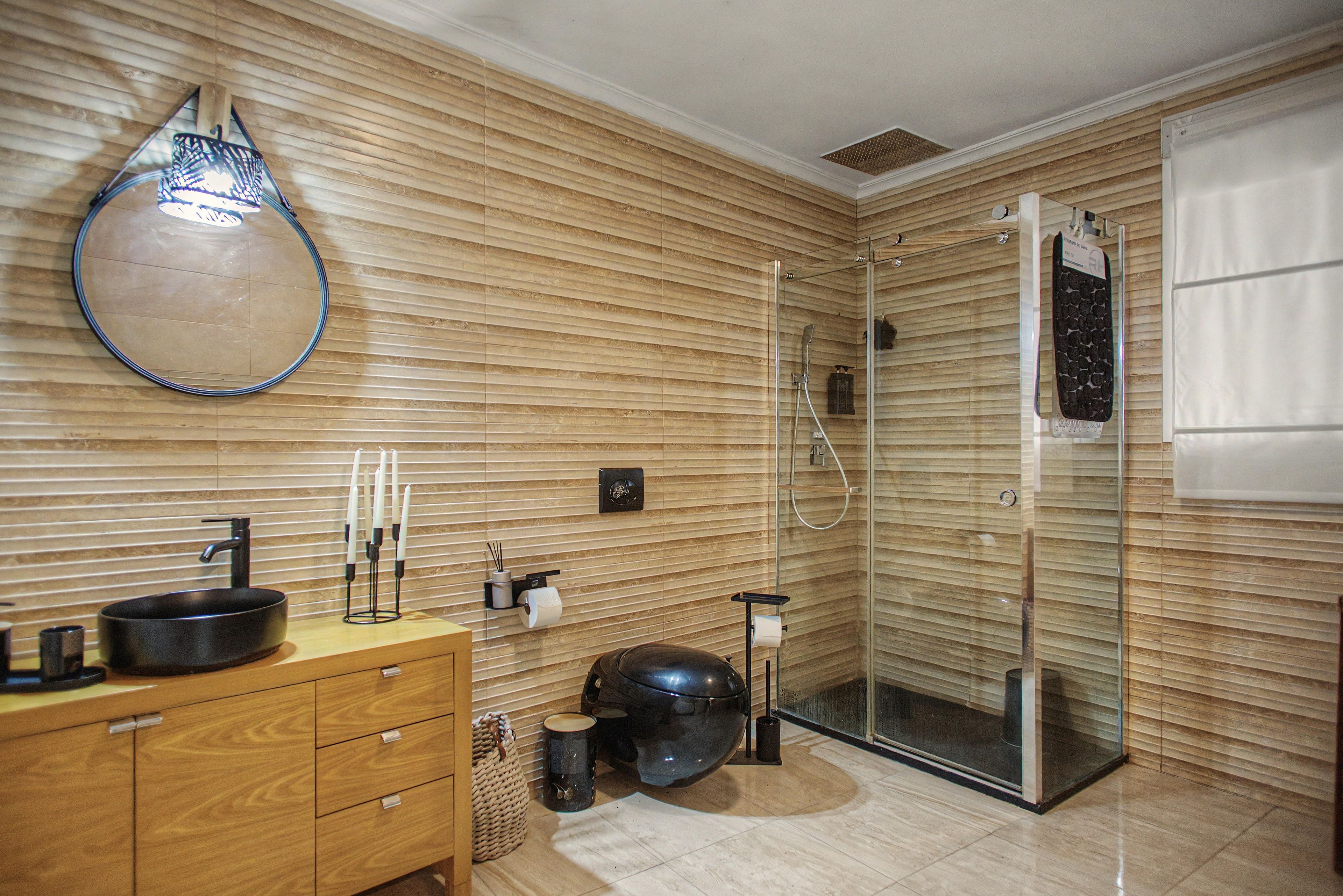 Een moderne badkamer met een houten wand, een ronde spiegel, een zwart wastafelmeubel en een douche met glazen wanden.