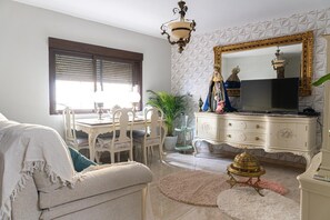 Une pièce comprenant une table à manger, des chaises, un canapé, un téléviseur, une commode et un lustre.