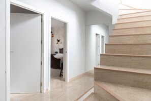 A modern interior with a staircase, a hallway, and a bedroom with a bed and nightstand.