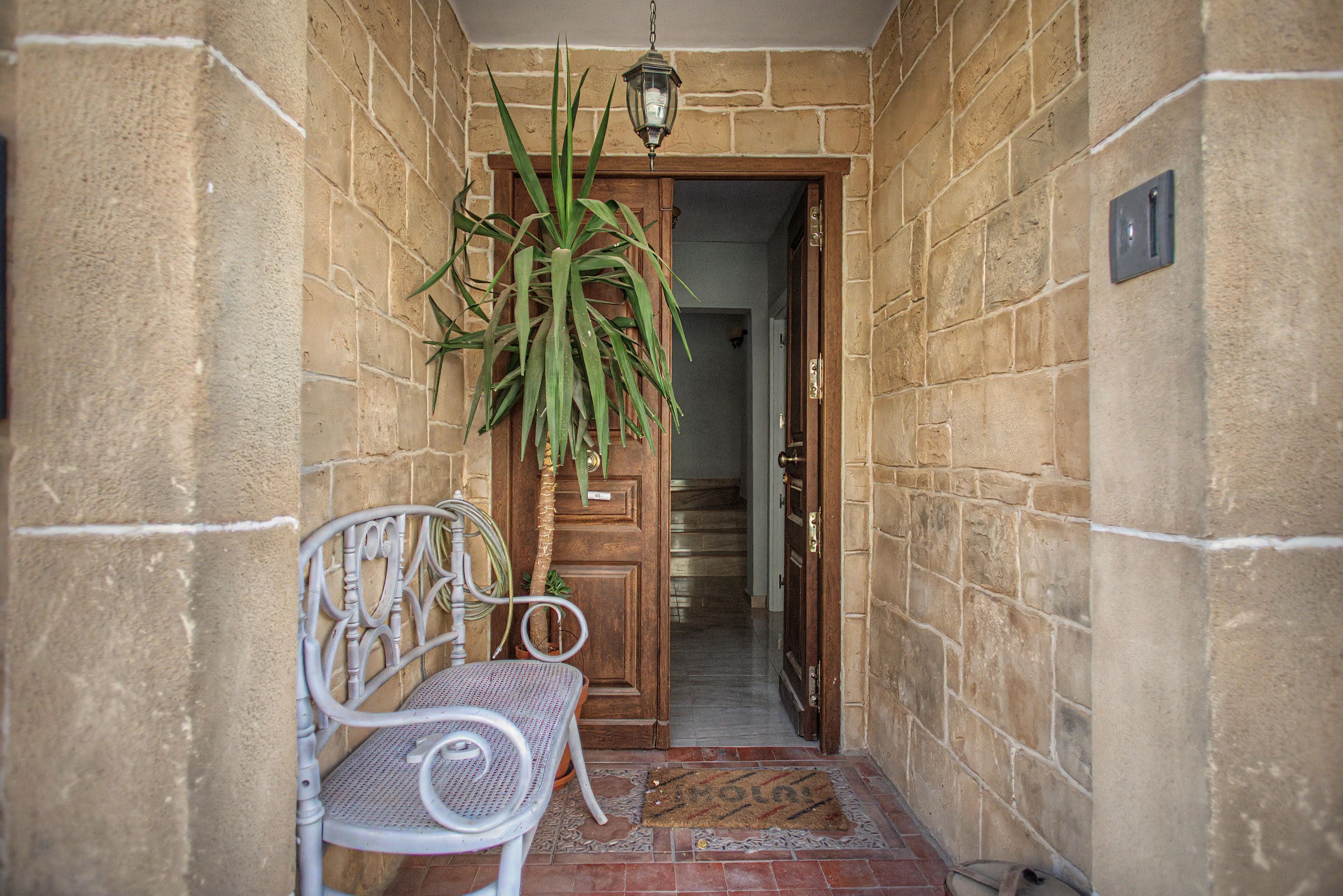 A narrow entrance with a wooden door, a metal bench, and a hanging plant.