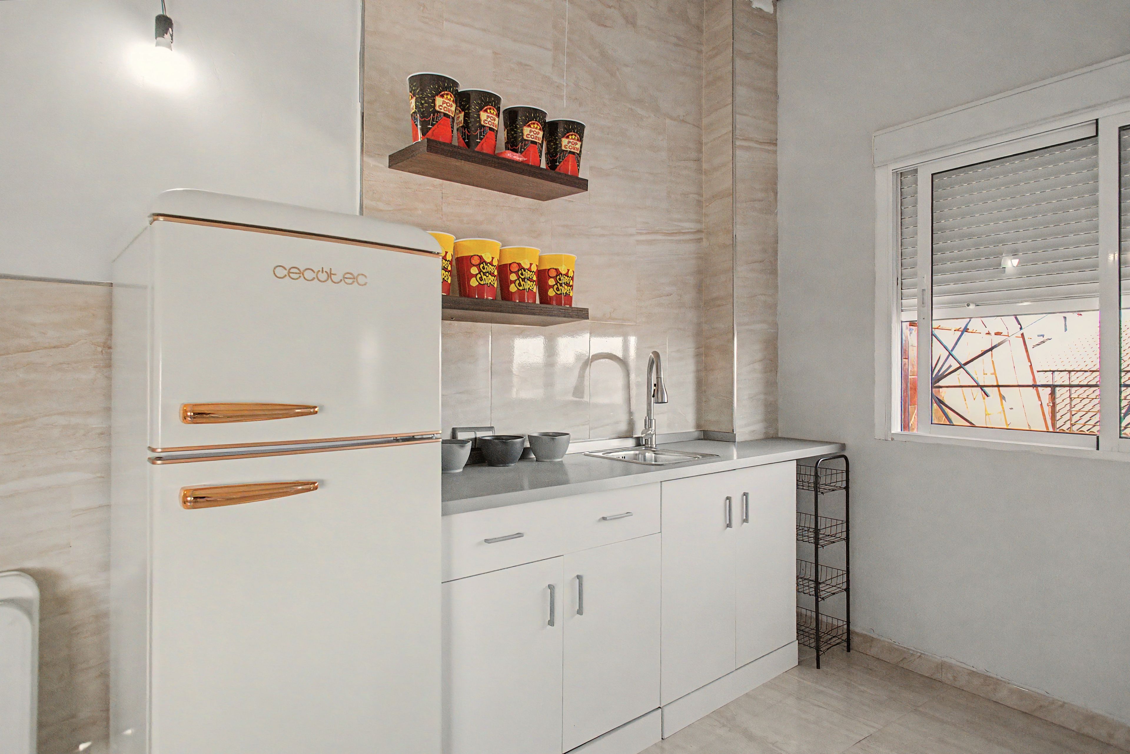 A modern kitchen with white cabinetry, a built-in oven, and a window with blinds.