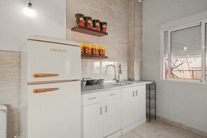 Une cuisine moderne avec des meubles blancs, un four encastré et une fenêtre équipée de stores.