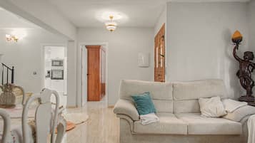A living room with a sofa, a dining table, and a kitchen in the background.