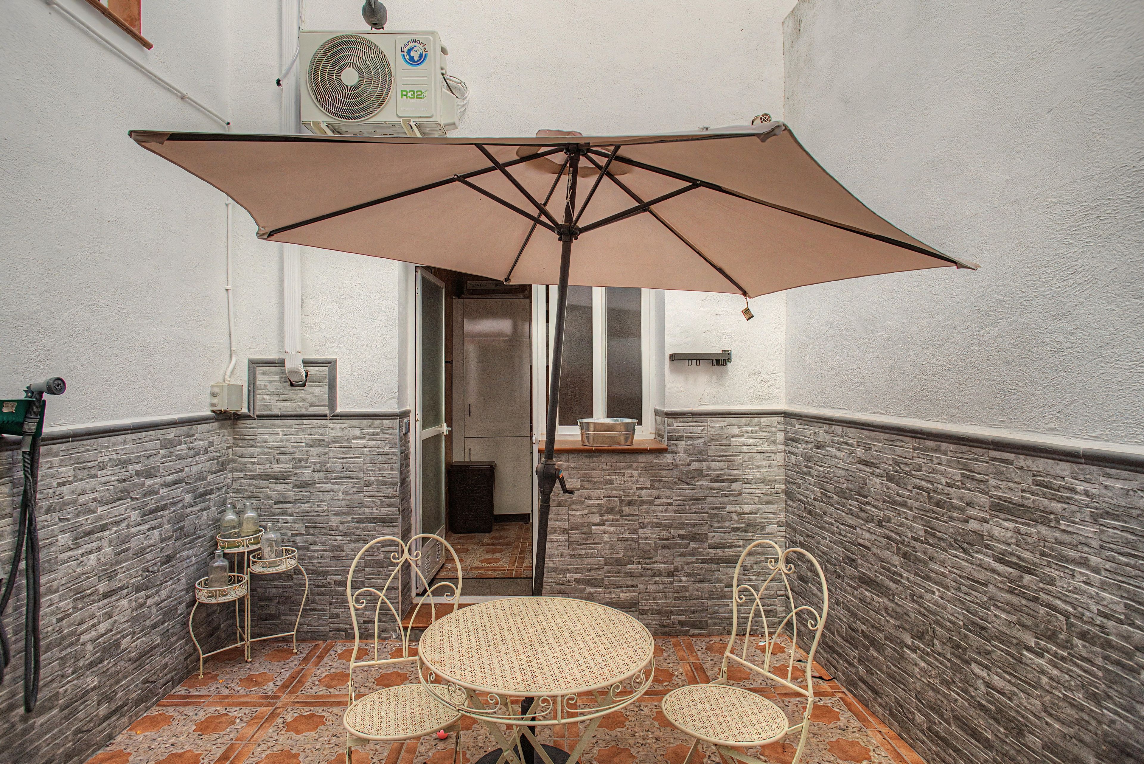 Un pequeño espacio al aire libre con mesa, sillas, una sombrilla y un equipo de aire acondicionado instalado en la pared.